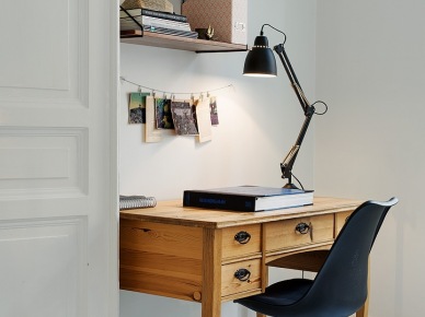 Drewniane miodowe biurko z wiszącymi pólkami na białej scianie w aranżacji mieszkania,czarne krzesło na krzyżakach i czarna lampa biurkowa z przegubami (26137)
