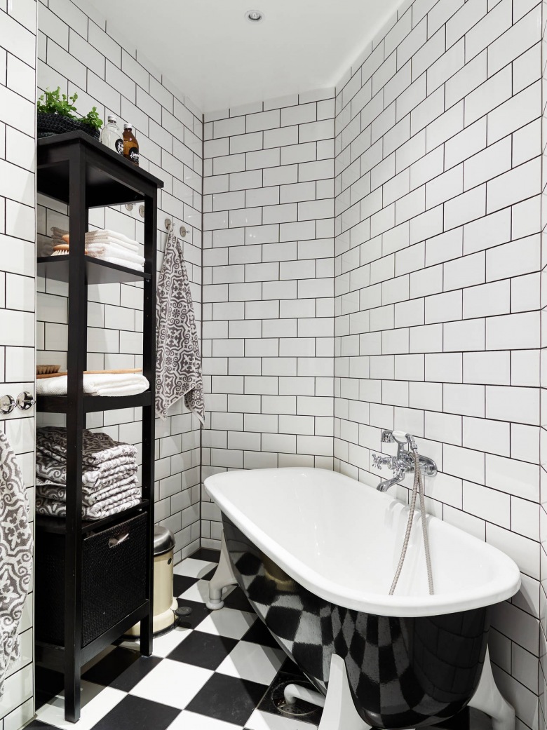 Biała glazura cegiełka na ścianie w łazience, posadzka w szachownicę ,wolnostojaca czarna wanna i czarne etażeki z pólkami (26984)