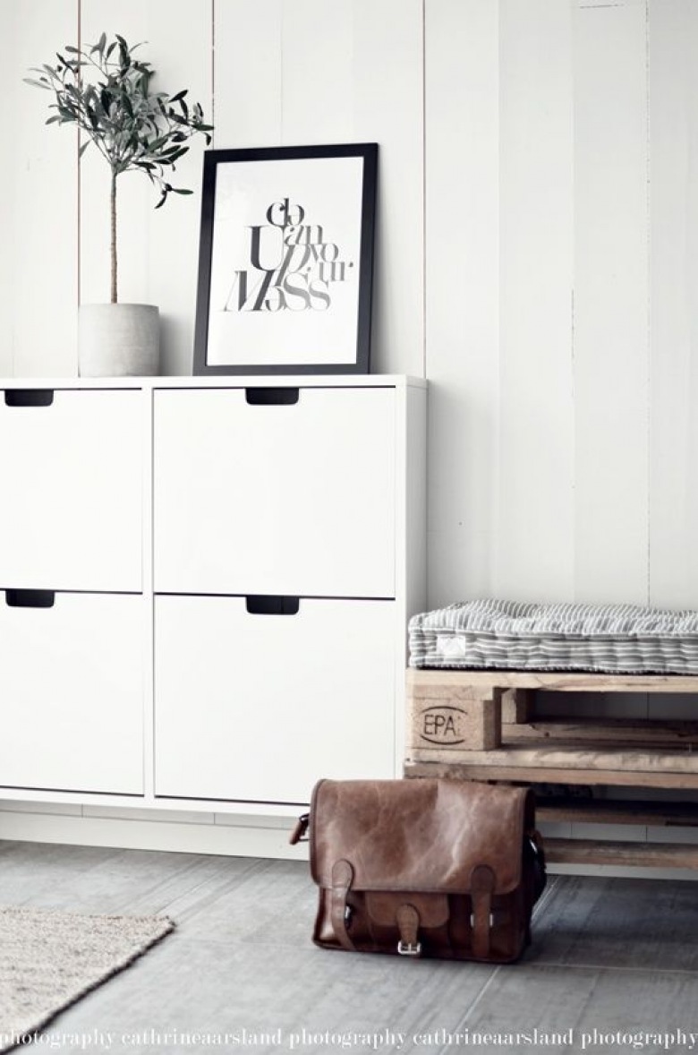 Biała wisząca szafka na buty,siedzisko z drewnianej palety,pikowane poduszki w paski,białe panele na ścianie,szara podłoga z desek w przedpokoju w stylu skandynawskim (25790)