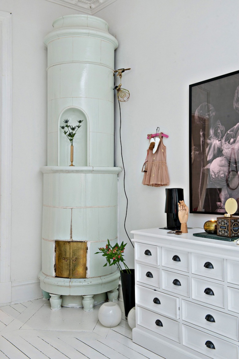 Okrągły ceramiczny piec skandynawski, biała komoda z szufladkami i nowoczesna grafika na ścianie w salonie (28414)