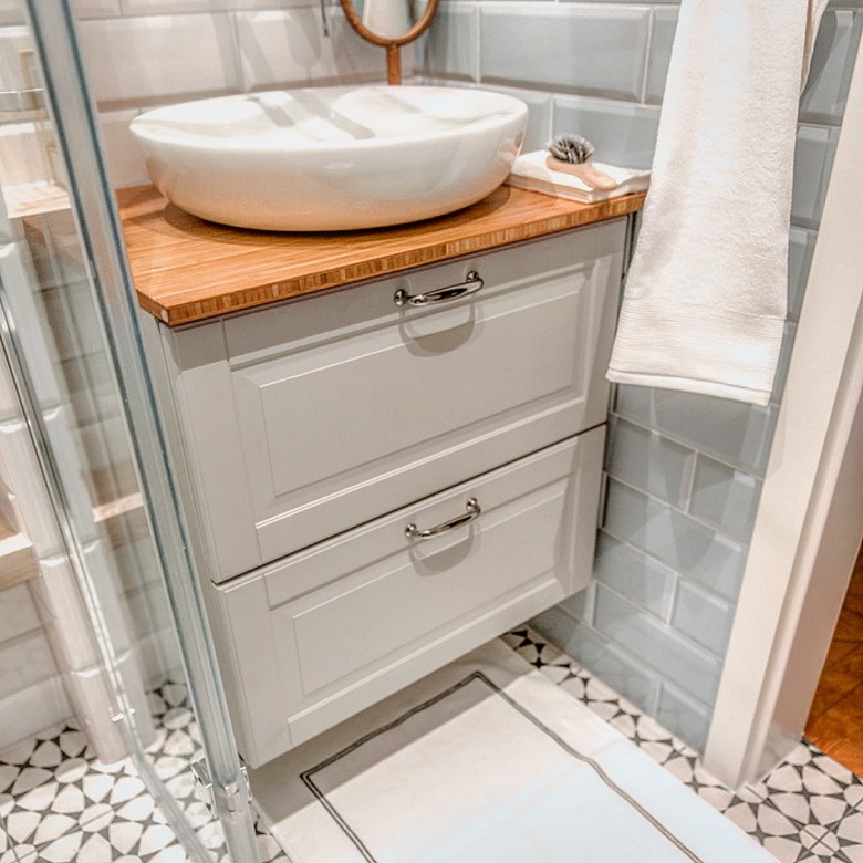 Wzorzyste płytki w łazience idealnie współgrają z szafką pod umywalką. Oryginalny motyw na podłodze urozmaica przestrzeń. Biały kolor umywalki pasuje z kolei do innych elementów. Całość jest bardzo harmonijnie...