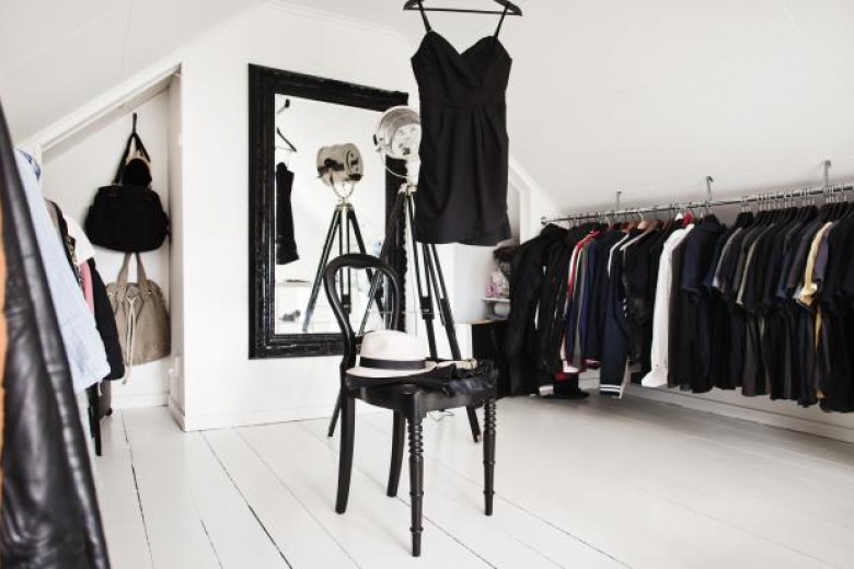 Czarne stylowe lustro na białej ścianie w garderobie z odkrytymi wieszakami,czarne giete krzesło na białych deskach podłogi (26348)