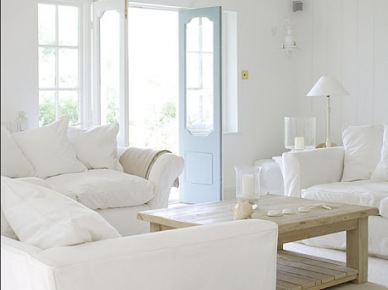 Aranżacja salonu z białymi sofami,drewnianym stolikiem ,wiklinowym koszem i niebieskimi drzwiami (21731)