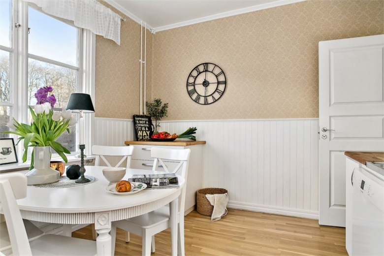 Stylowa beżowa tapeta na ścianie w jadalni,białe drewniane lamperie i biały okrągły stół z krzesłami w stylu skandynawskim (27687)