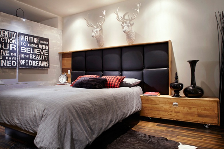 Nowoczesne drewniane łóżko z czarnym pikowanym zagłówkiem, typografie i białe głowy jelonków w męskiej sypialni (24480)