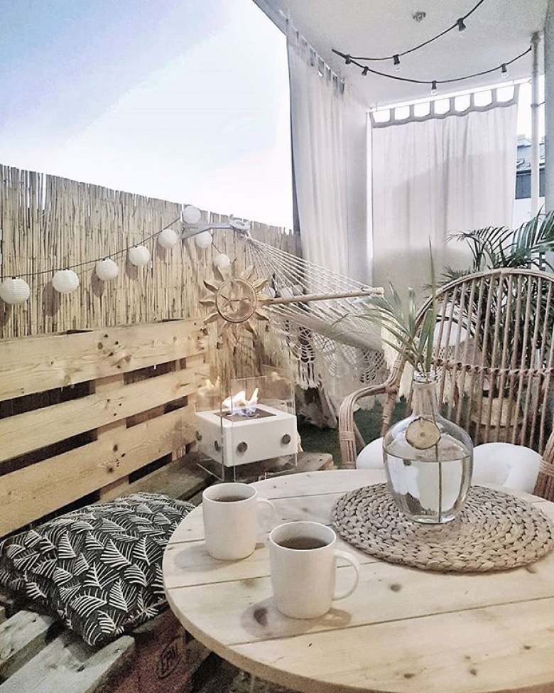 Girlanda świetlna na balkonie nadaje całości romantyczny charakter. Oprócz siedziska z palet znajduje się tu także stoliczek z drewna oraz zawieszony w głębi tarasu hamak....