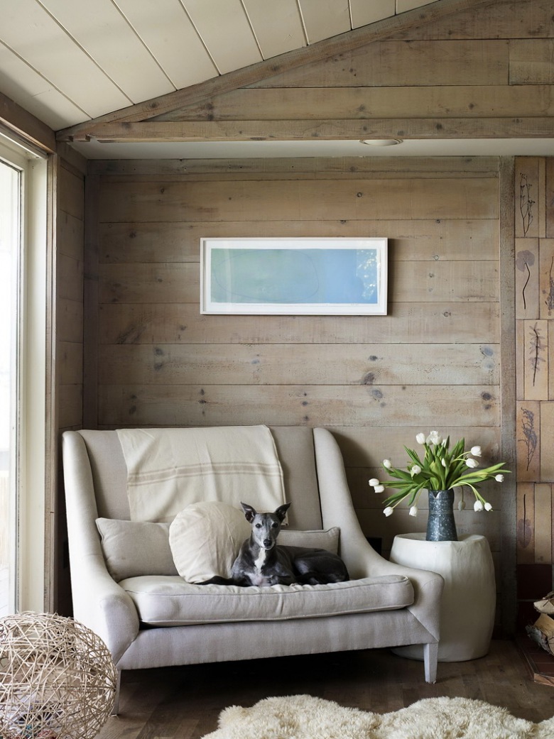 Nowoczesna kanapa w tapicerce złamanej bieli,futrzak i szerokie proste deski na ścianie w aranżacji kącika wypoczynkowego w wakacyjnym domu (25339)