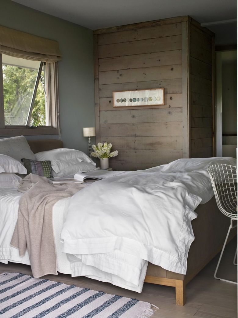 Lniana roleta rzymska,drewniane łóżko,szerokie szarawe deski na ścianie i ażurowy biały foteli z metalu (25343)