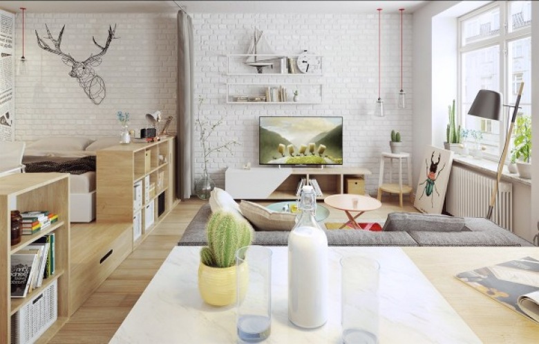 Białe cegły na ścianie idealnie wpisują się w skandynawski charakter mieszkania i tworzą we wnętrzu oryginalny klimat. Po lewej stronie wydzielono część sypialnianą za pomocą podwyższenia i sprytnego oddzielenia łóżka od salonu niskimi...