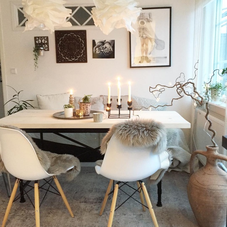 Biały stół z białym krzesłami w skandynawskim stylu otoczono wieloma dekoracjami. Warto zwrócić uwagę na galerię ścienną, a także na rozmaitość materiałów, które dodają jadalni...