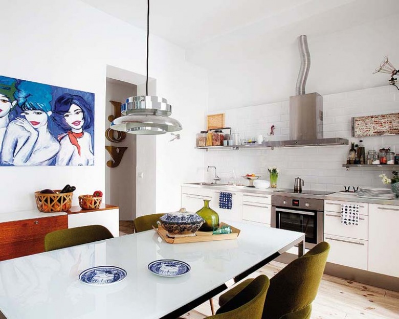 Jasna drewniana podłogo w białej nowoczesnej kuchni  to świetne rozwiązanie.Zielone krzesła i obraz wprowadzają eklektyczny...