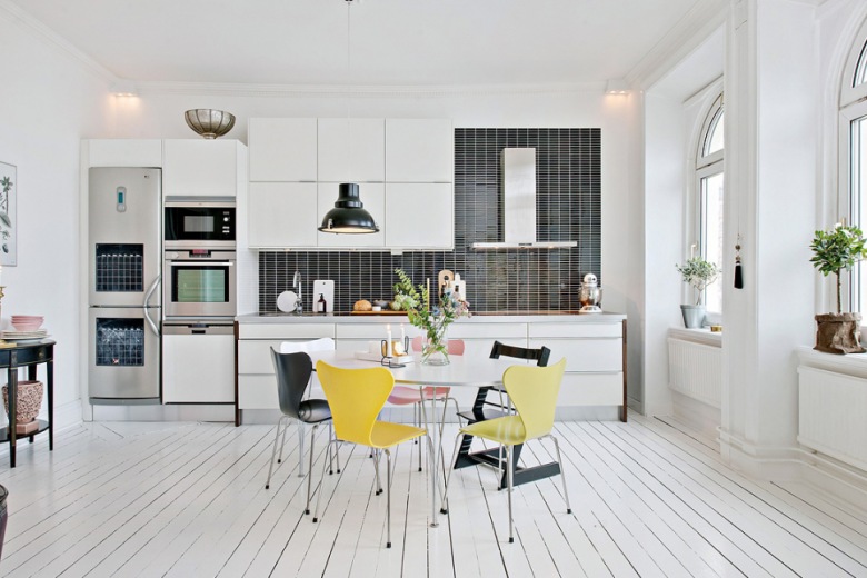 Biała kuchnia skandynawska z czarną glazurą na ścianie, okragłym stołem , żółtymi, czarnymi  i różowymi krzesłami (28408)