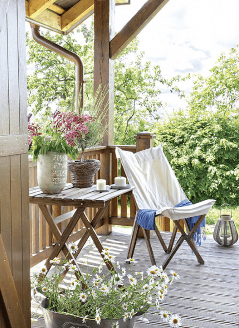Drewniany stolik na krzyżaku i drewniany fotel skandynawski z białym płótnem,lampiony i rustykalne osłonki na kwiaty na wiejskiej werandzie (24840)