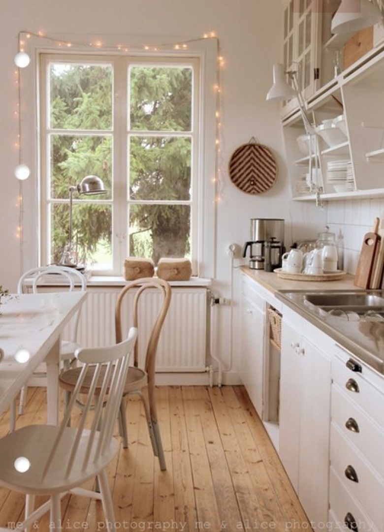 Okno w białej kuchni przystrojone światełkami pięknie dekoruje całe wnętrze.