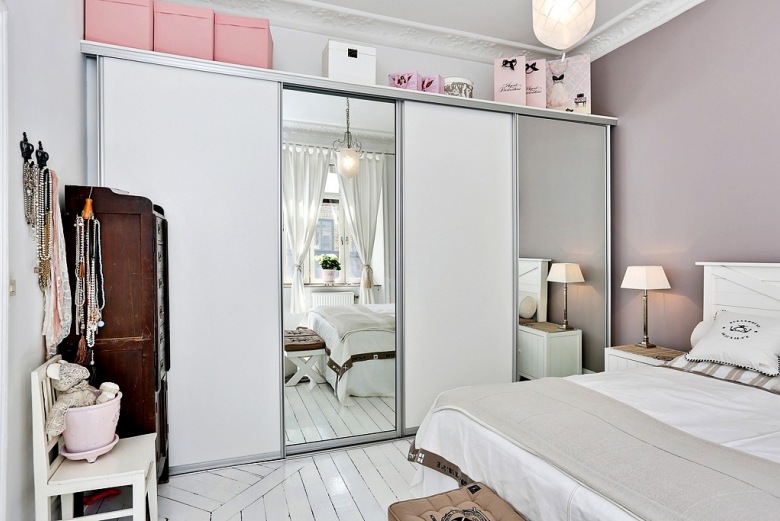 Biała szafa z przesuwnymi lustrzanymi drzwiami i różowe pudełka w aranżacji skandynawskiej sypialni (24389)