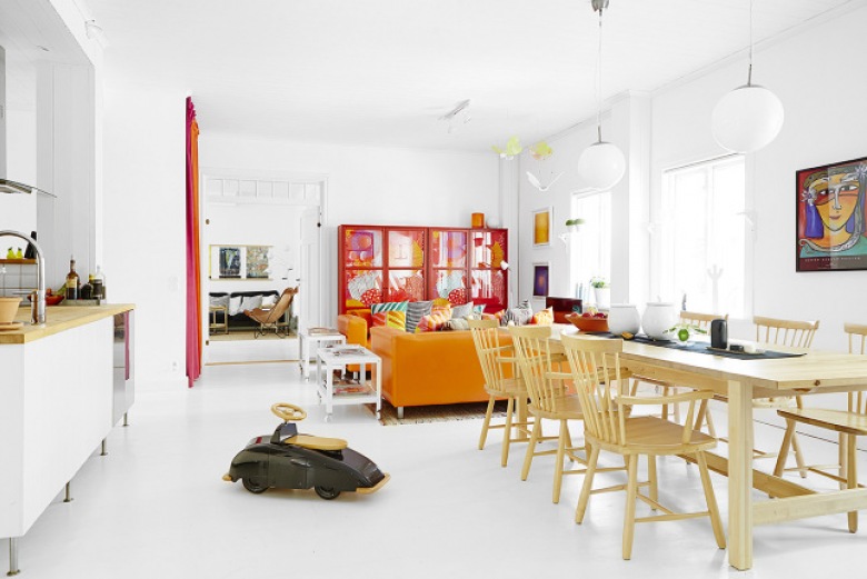 Czerwony regała,pomarańczowa sofa i drewniany stół z krzesłami w otwartym salonie (24655)