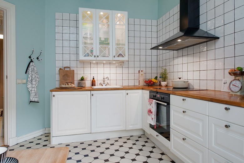 Biała kwadratowa glazura na turkusowej ścianie w białej kuchni skandynawskiej z czarnym okapem i bialo-czarną terakotą na podłodze (25871)