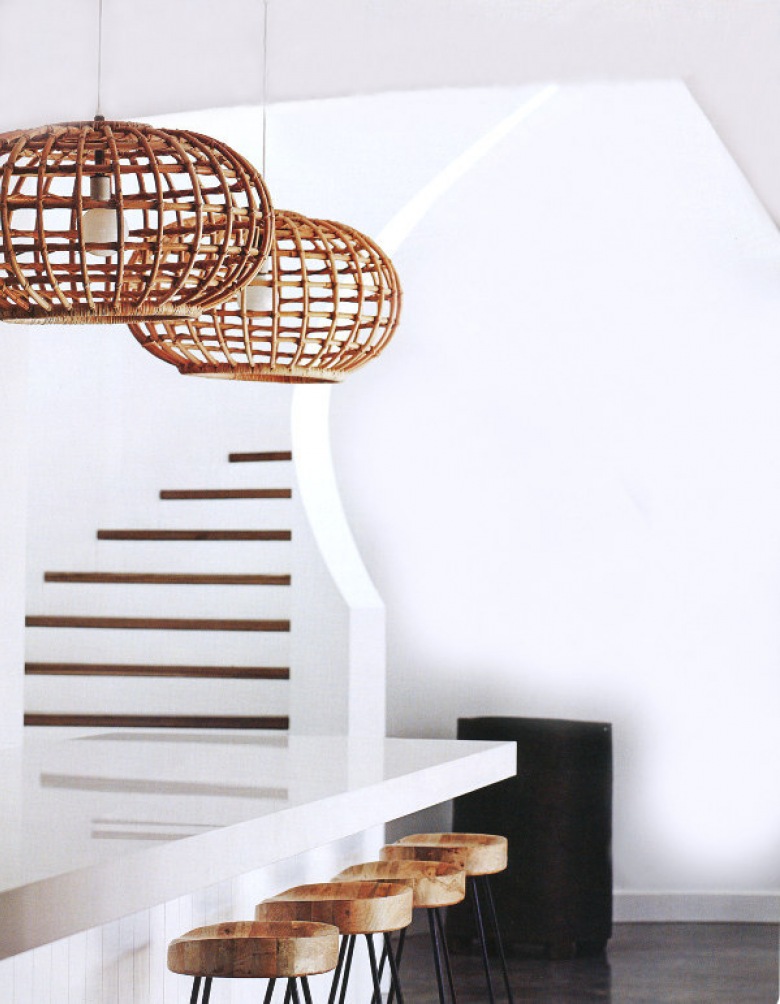 Ażurowe lampy z bambusa nad biała lada kuchenną przy białych schodach z drewnianymi opaskami (25139)