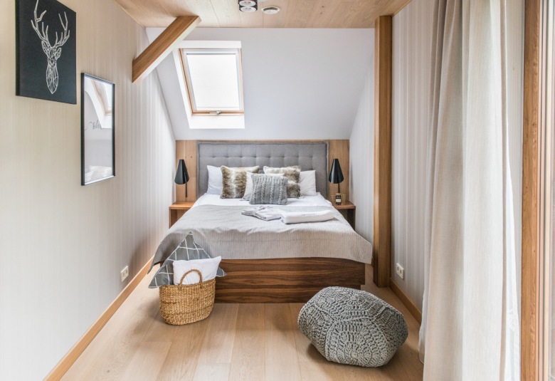 Okno dachowe zapewnia dostęp naturalnego światła, chociaż kolorystyka wnętrza i tak jest dość jasna. Drewniane łóżko z pikowanym wezgłowiem stanowi główny element aranżacji sypialni na...