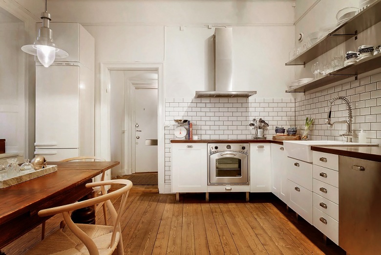 Biała kuchnia w stylu skandynawskim z drewnianymi blatami, podłogą z desek i drewnianym stołem w brązowo-miodowym kolorze (27099)