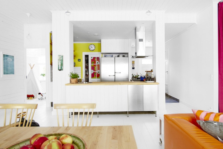 Biala kuchnia z drewnianymi blatami i żółtą ścianą w otwartym widoku na jadalnię i salon (24656)
