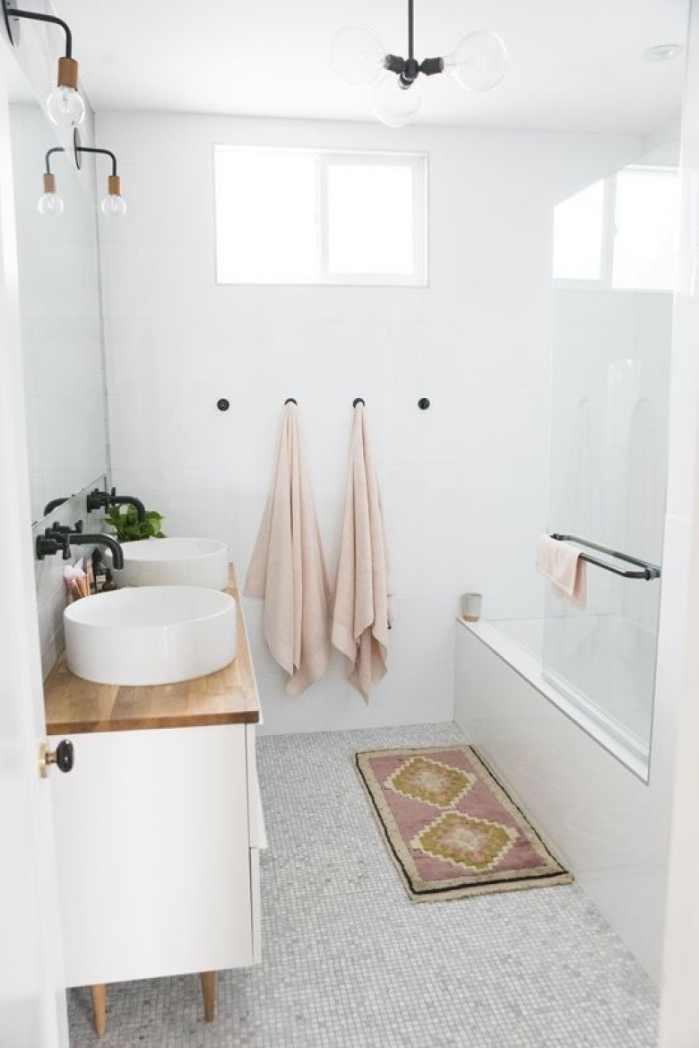 W niewielkiej łazience znajduje się kilka dekoracyjnych elementów. Jednym z nich jest mały dywanik ze wzorem przed wanną. Drewniany blat ładnie prezentuje się z bielą, co podkreśla inspirację skandynawskim...