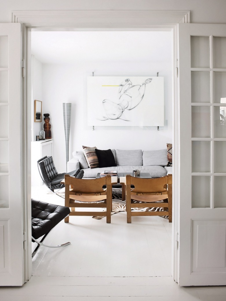 Nowoczesne grafiki,drewniane skandynawskie fotele,pikowany czarny fotel na metalowych nóżkach,szara sofa i biała podłoga w salonie (27017)
