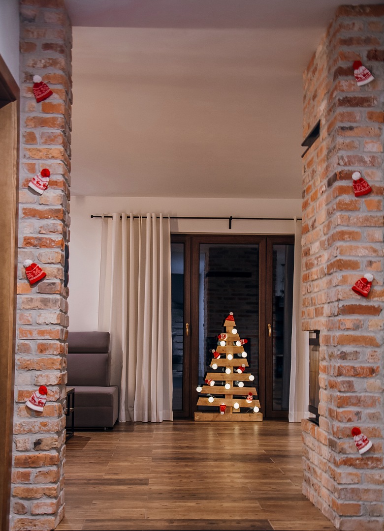 Niezwykle ciekawy pomysł na świąteczną choinkę, czyli drewniane drzewko przyozdobione lampkami. Czerwone drobne dekoracje przymocowane do cegieł podkreślają świąteczny klimat, jednocześnie nie zaburzając minimalistycznej koncepcji wystroju...