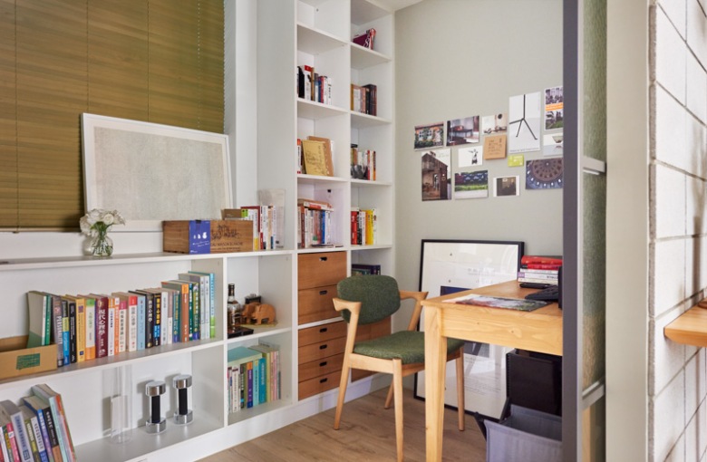 Mały pokój biurowy jest funkcjonalnie urządzony. Na dłuższej ścianie ustawiono białe regały, na których właściciele przechowują...