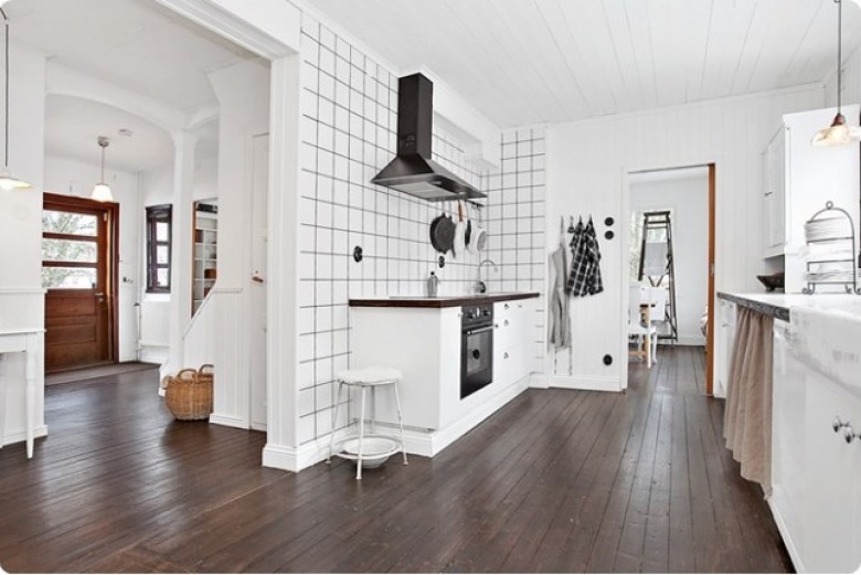 Biała kwadratowa płytka z czarnymi spoinami na ścianie kuchennej z czarnym okapem, brązowa ciemna podłoga z desek na podłodze w białej kuchni (27873)