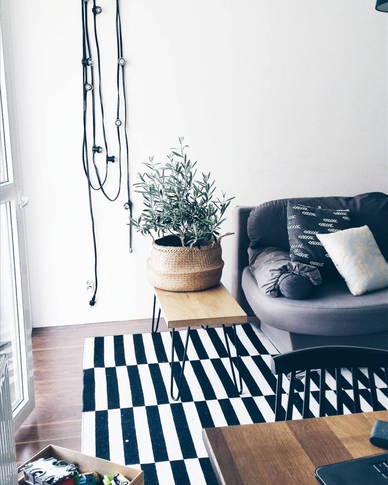 W salonie uwagę przykuwa do siebie kilka elementów, szczególnie pasiasty dywan w biało-czarnym kolorze. Połączenie drewna w postaci mebli i doniczkowych roślin w przyjemny sposób podkreśla naturalny aspekt...
