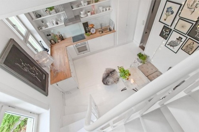 Widok z góry na biała kuchnię z drewnianymi blatami,biała podłogą i biało-czarnymi fotografiami i grafikami (24575)