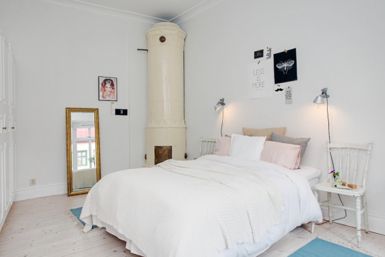 Ceramiczny okragły piec skandynawski,złocone stojace lustro,srebrne lampki przy białym łóżku w sypialni z turkusowymi dywanikami (26466)