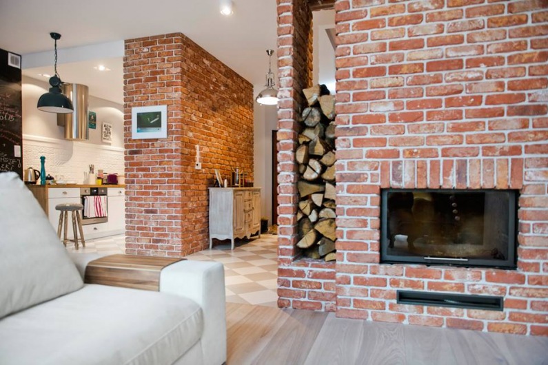 Czerwone cegły łączą aranżację salonu z aranżacją kuchni, zapewniając spójność w części dziennej domu w skandynawskim...