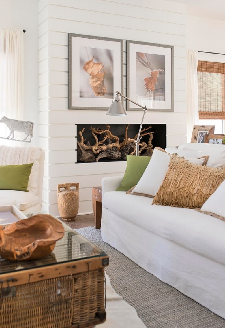 Białe panele z drewna na ścianie z kominkiem,dekoracje z korzeni,biala sofa z beżowymi i zielonymi poduszkami,wiklinowa skrzynia ze szklanym blatem w roli stolika w salonie (26161)