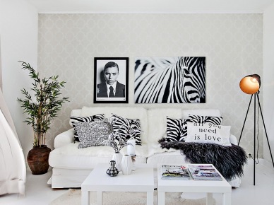 Czarno-białe fotografie postaci i zebry,gaficzne poduszki,czarna lampa na trójnogu,glinaiany wazon i biala sofa w salonie (24743)