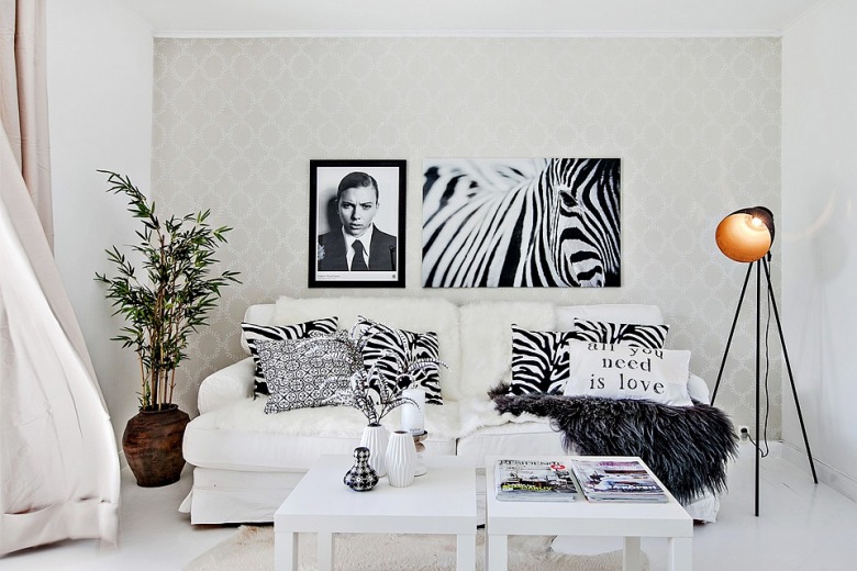 Czarno-białe fotografie postaci i zebry,gaficzne poduszki,czarna lampa na trójnogu,glinaiany wazon i biala sofa w salonie (24743)