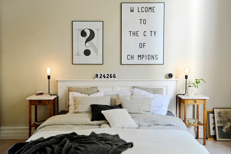 Typografie i grafiki na ścianie w skandynawskiej sypialni z białym łóżkiem i stylowymi drewnianymi stolikami nocnymi (23453)