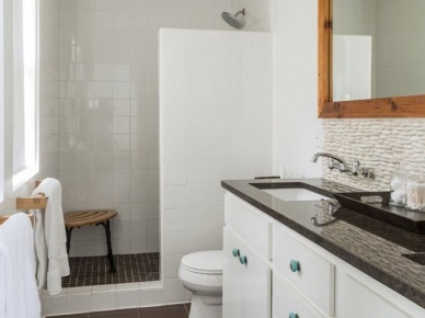 Higienicznie biała łazienka ocieplona drewnianą ramą lustra i brązową podłogą oraz blatem w takim samym kolorze. Duża ilość szafek i szuflad pozwala na utrzymanie...