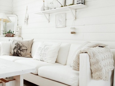 Skandynawska biała kanapa, białe drewniane pólki na scianie i biały drewniany stół w wiejskim salonie (25584)