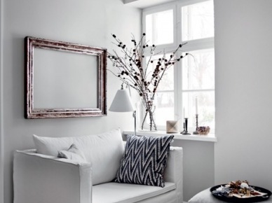 Minimalistyczna biała sofa z szarym podnóżkiem,drewniane ramy vintage i drewniany taboret w salonie przy oknie (27406)