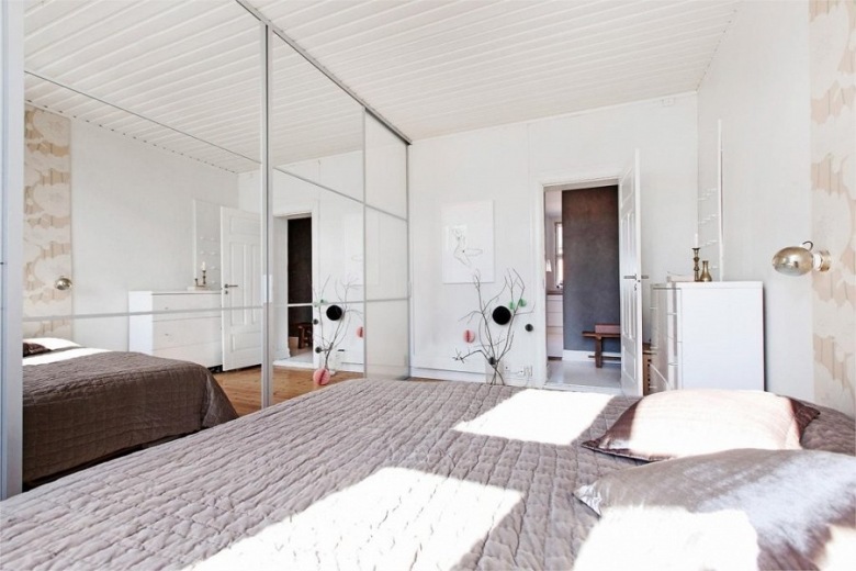 Aranżacja białej sypialni z szarą narzutą na łóżku i lustrzanymi szafami z przesuwnymi drzwiami (24570)