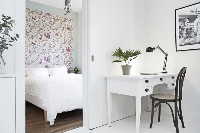 Skandynawskie białe biurko z szufladami,czarne gięte krzesło z drewna,biała podłoga i kwiatowa tapeta na ścianie przy łóżku (27861)