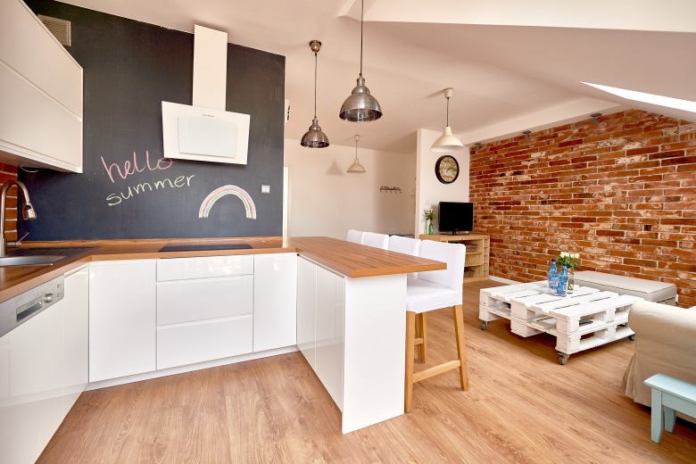 Biała zabudowa w kuchni pozwala wyeksponować ciekawe rozwiązania w bardziej nasyconych kolorach. Czerwone cegły w tle oraz czarna farba tablicowa na ścianie znacząco zdobią wnętrze....