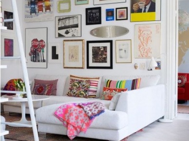 Pomysł na kolorową galerię na białej ścianie z grafik i plakatów i róznobarwne poduszki na sofie w salonie (28057)