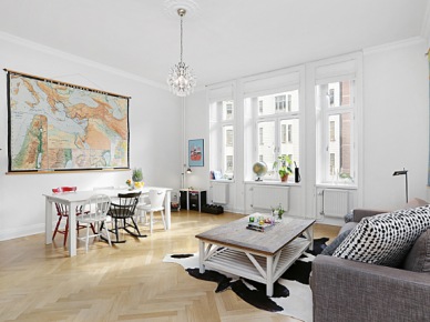 Mapa fizyczna świata na ścianie w salonie z białym stołem,różnymi krzesłami, szarą sofą i drewnianym białym stoliek kawowym w stylu shabby (26753)