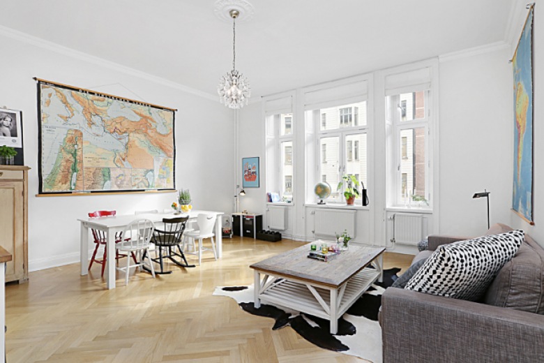 Mapa fizyczna świata na ścianie w salonie z białym stołem,różnymi krzesłami, szarą sofą i drewnianym białym stoliek kawowym w stylu shabby (26753)