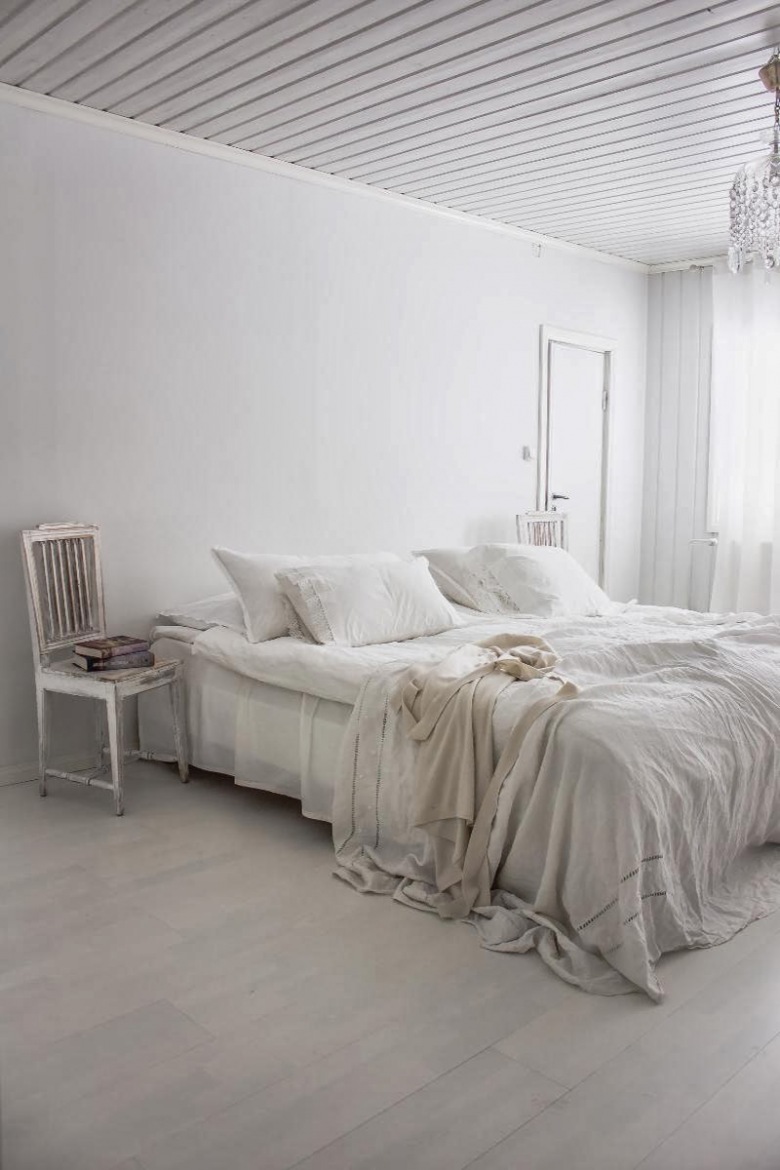 Biała sypialnia z patynowanym krzesłem, kryształowym żyrandolem i białą dekoracją łóżka (21680)