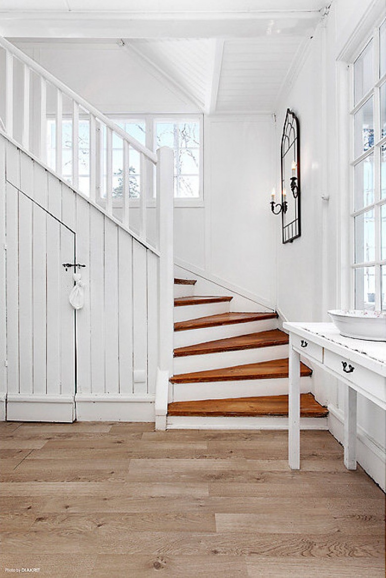 Biała konsolka z lustrem przy    drewnianych  schodach w domu (21960)