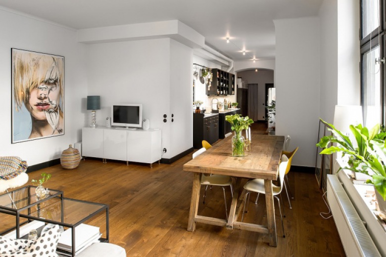Drewniana podłoga,drewniany stół prostokatny z nowoczesnymi krzesłami,nowoczesny obraz i białe szafki w otwartym salonie z kuchnią i jadalnią (26449)